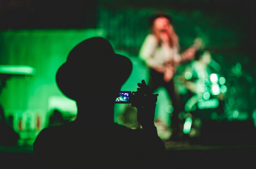 silhouette of man holding camcorder near woman singing on stage